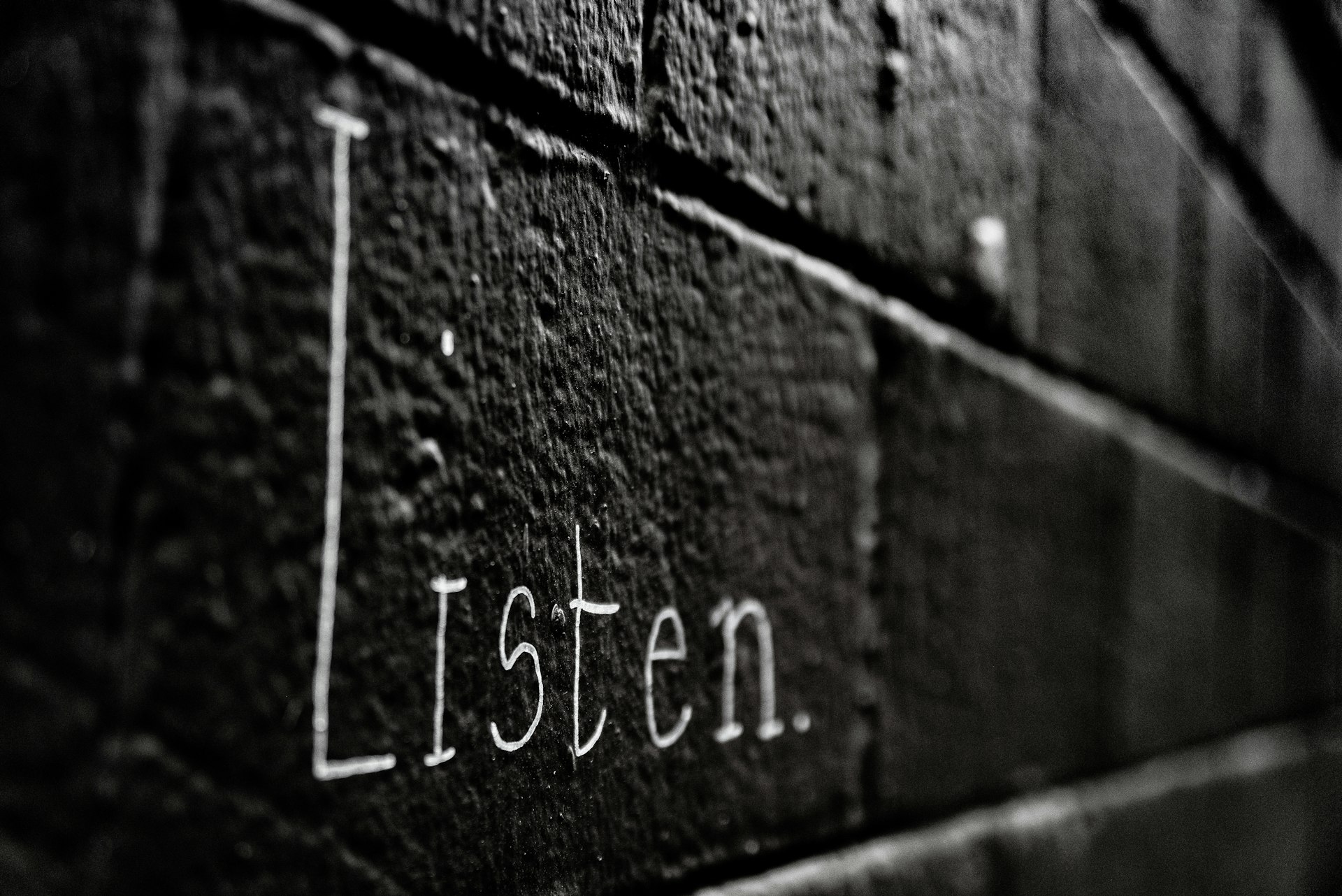 a black and white photo of the word listen written on a brick wall