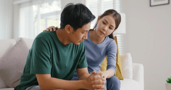 Người nữ đang vỗ vai và nắm tay người nam đang đăm chiêu