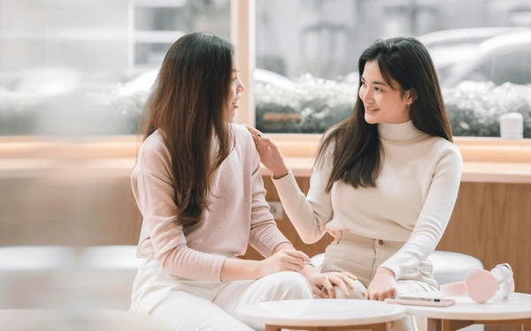 Một cô gái vỗ vai một cô gái khác tươi cười