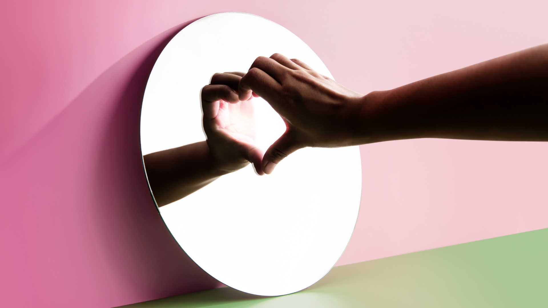 A hand make a heart with its reflection on the mirror